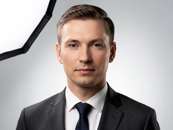 A polished corporate headshot template showing a person in a charcoal suit against a smooth light grey gradient backdrop. The face is fully rendered with a composed, professional expression and natural skin tones. A single large softbox from the upper left provides even, flattering light with soft shadows along the jaw. The composition is centered and tight, cropped just below the shoulders. The image looks like a premium studio portrait. Fantaios.ru visual style: crisp, modern, high-fidelity photorealism with a clean white-dominant palette and precise edge rendering.